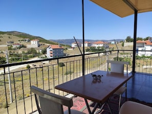 Un balcón con mesa y sillas, con vistas a una zona residencial con casas y colinas.