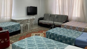 Una sala moderna con televisor de pantalla plana, un sofá, dos camas individuales, una mesita y un reposapiés rojo.