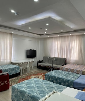 Una sala moderna con televisor de pantalla plana, un sofá, dos camas individuales, una mesita y un reposapiés rojo.