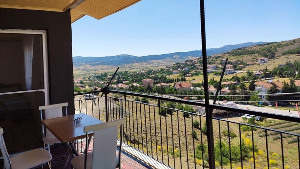 Un balcón con una mesa y sillas, con vistas a un paisaje rural con casas y colinas.