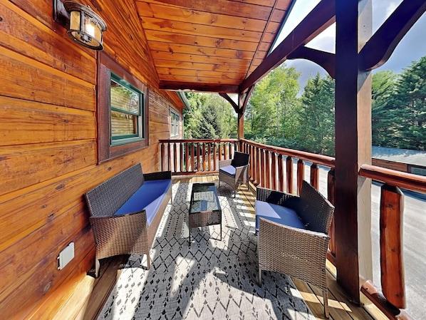 Une terrasse en bois, dotée de meubles en osier et d’une table en verre, qui offre une vue sur une zone boisée.