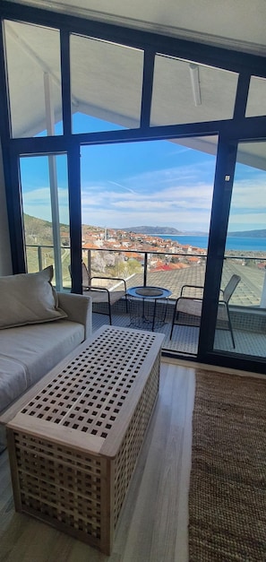 Una habitación con un ventanal grande, un sofá, una mesita y vistas a un pueblo costero.