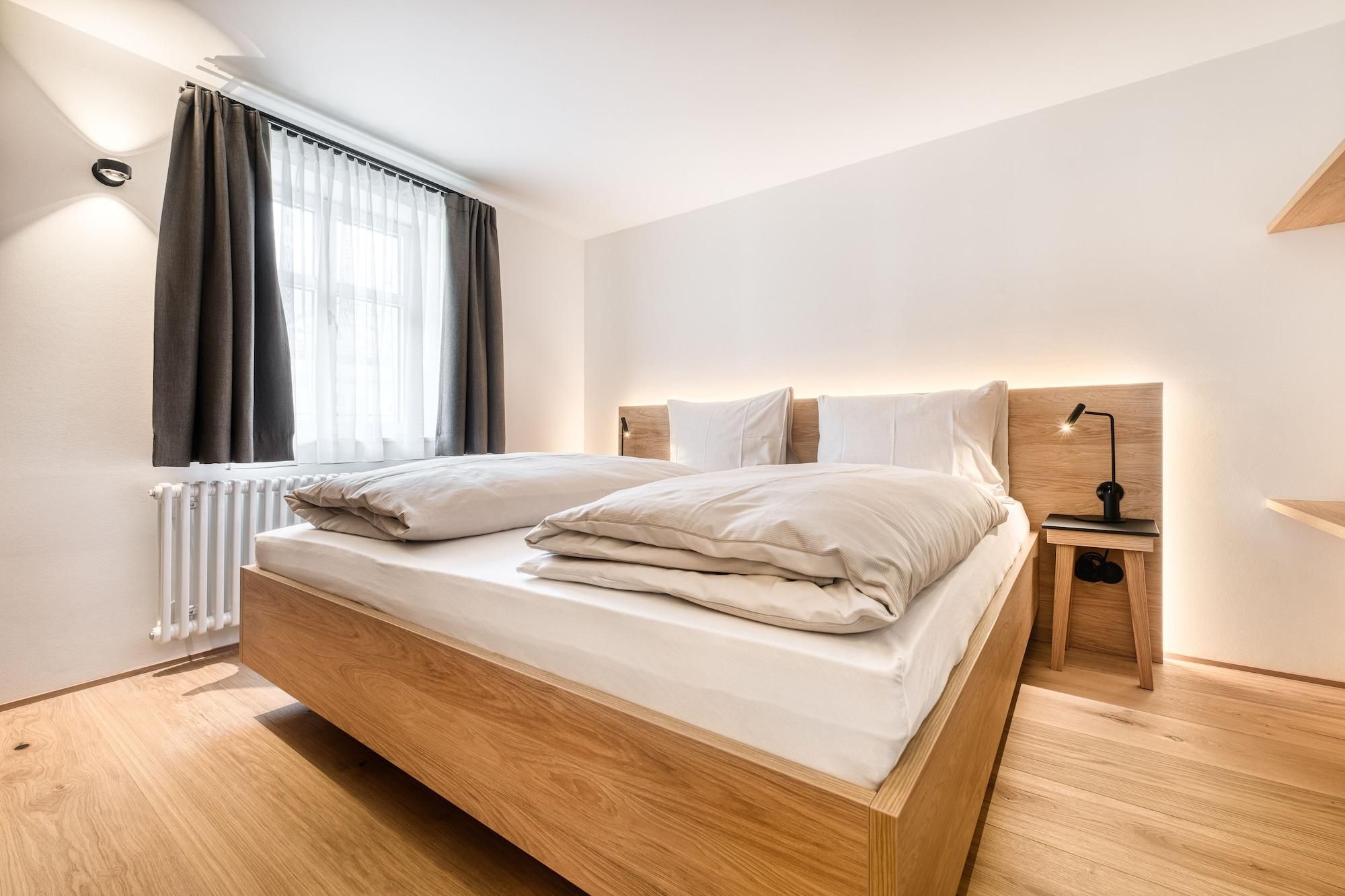 Un dormitorio moderno con una cama de madera, una mesita de noche con una lámpara y una ventana con cortinas.