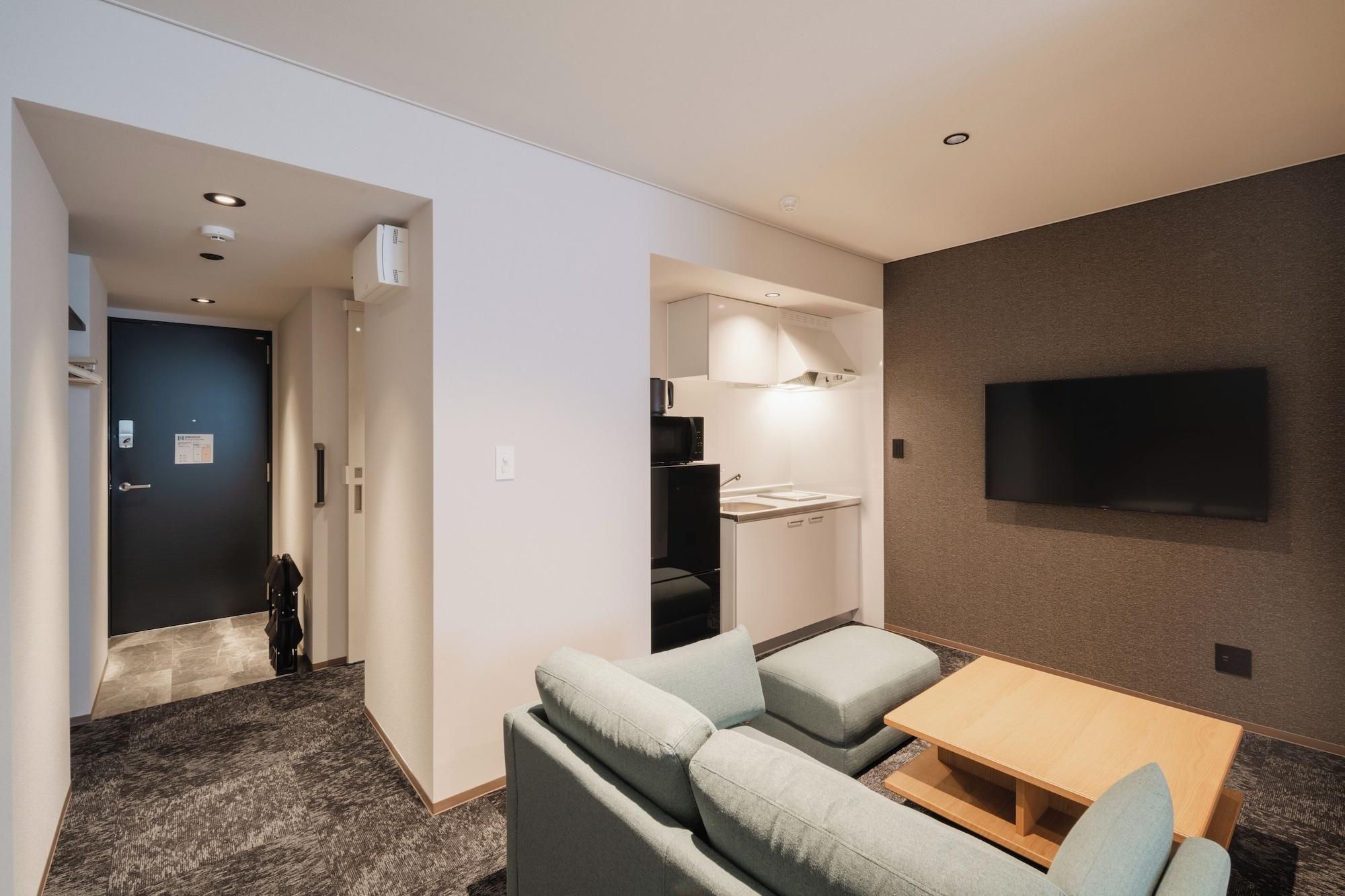 Habitación de hotel con sofá, una mesita, televisión montada en la pared y un espacio con kitchenette.