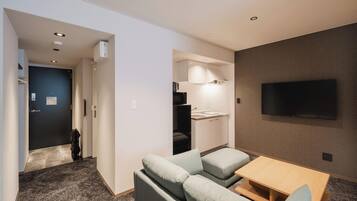 Habitación de hotel con sofá, una mesita, televisión montada en la pared y un espacio con kitchenette.