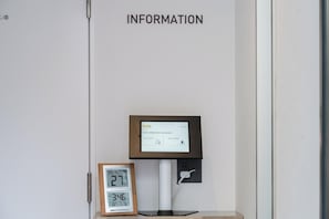 Digitaalinen infopiste, jossa on näyttö, jolta näkyvät hotellin tiedot, kello ja sen yläpuolella oleva kyltti, jossa lukee: ”TIETOJA”.