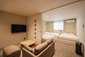Hotellihuone, jossa on sohva, televisio, pieni pöytä ja kaksi sänkyä.