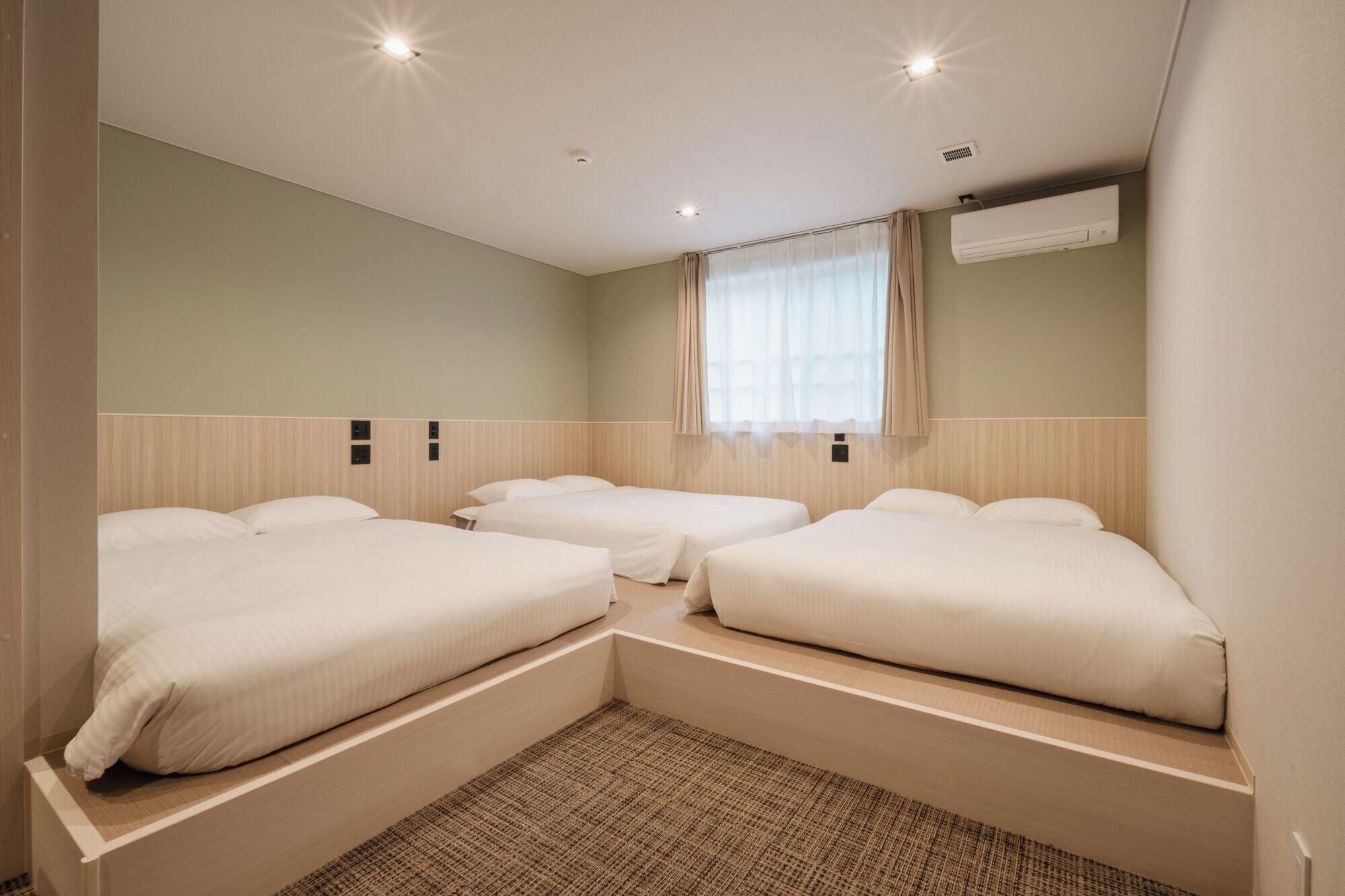 Habitación de hotel con dos camas individuales, un ventanal con cortinas, un equipo de aire acondicionado y una alfombra texturizada.
