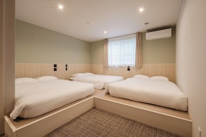 Hotellihuone, jossa on kaksi erillistä sänkyä, suuri ikkuna, jossa on verhot, ilmastointilaite ja kuvioitu matto.