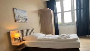 Ein Hotelzimmer mit Bett, Nachttisch mit Lampe, einem Gemälde an der Wand und einem Fenster mit Vorhängen.