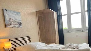 Ein ordentlich bezogenes Bett mit Holz-Kopfteil, einer Nachttischlampe und einem Gemälde an der Wand.