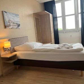Uma cama bem arrumada com cabeceira de madeira, luminária de cabeceira e um quadro na parede.