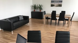 Ein moderner Büroraum mit einem schwarzen Ledersofa, einem Esstisch mit Stühlen und einem Laptop auf einem Holztisch.