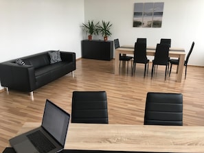 Espaço de escritório moderno com sofá de couro preto, mesa de jantar com cadeiras e um laptop em uma escrivaninha de madeira.