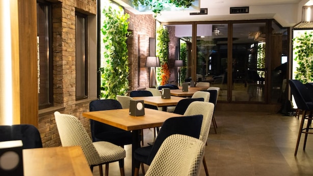 An indoor dining area with brick walls, green plants, and a mix of wooden and upholstered tables and chairs. - Hotel City In (Kocani)