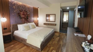 A modern hotel room with a large bed, wooden flooring, a mounted TV, and a bathroom visible through an open door. - Hotel City In (Kocani)