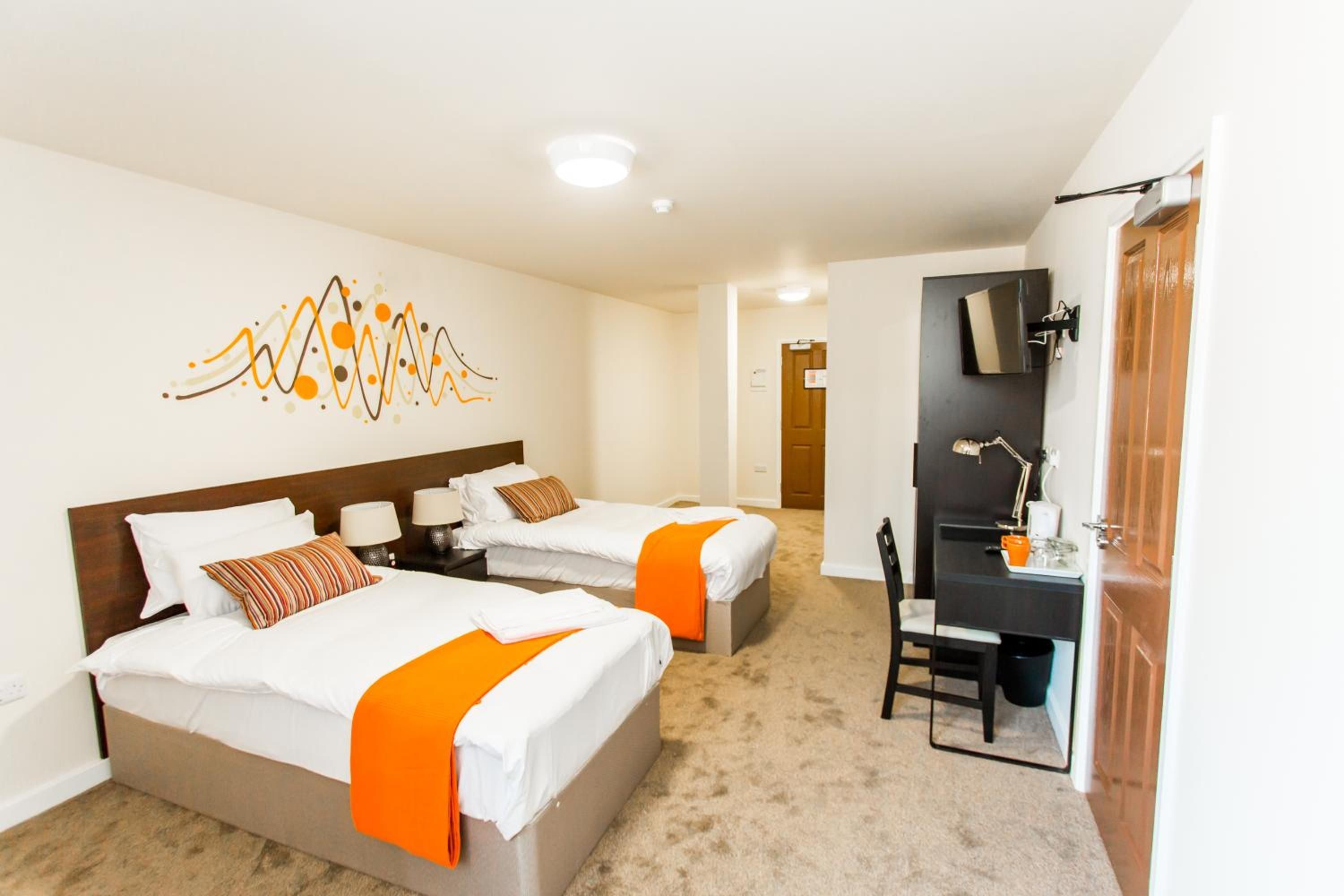 A hotel room with two beds, a desk, a chair, and a television.