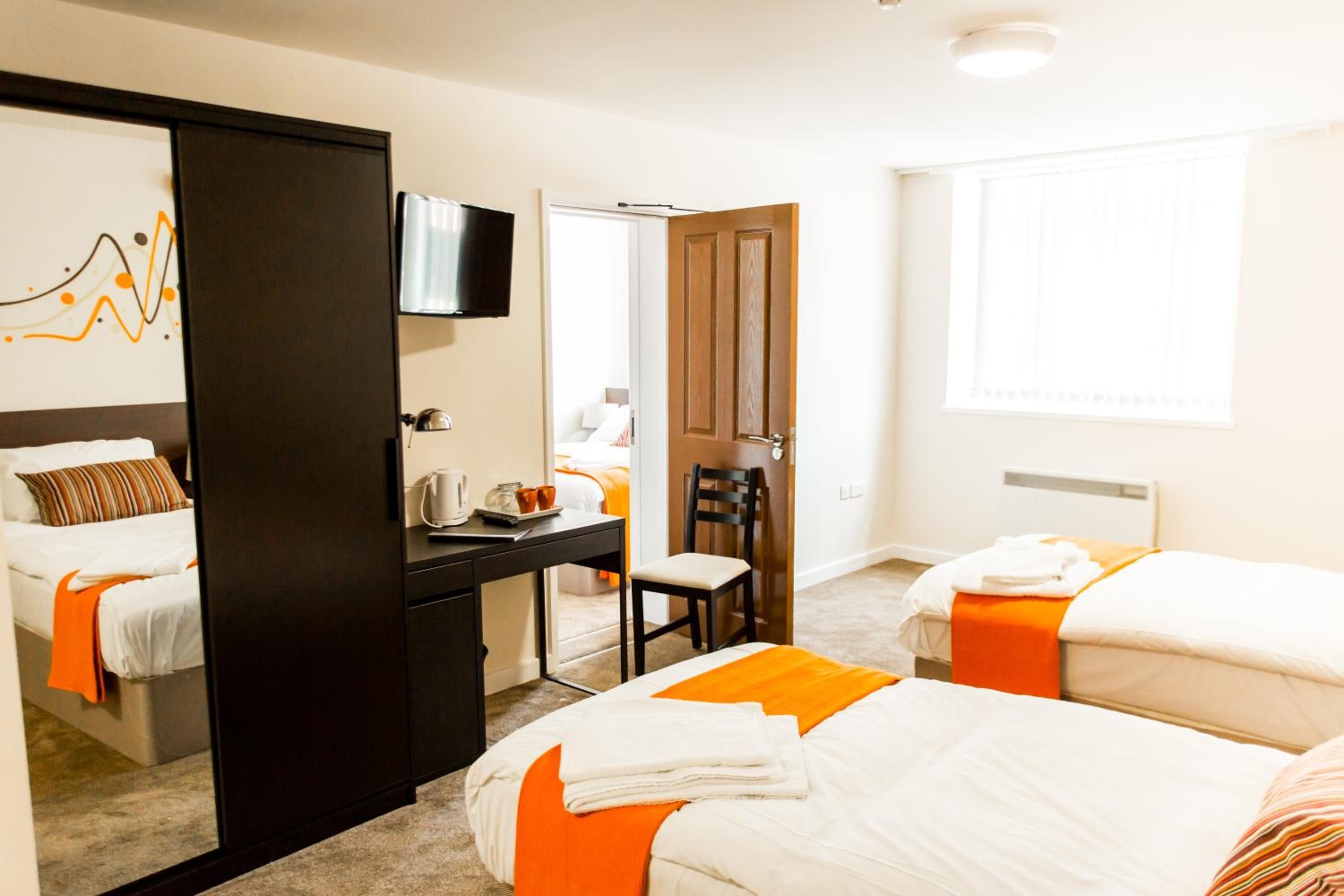 A hotel room with two beds, a desk with a chair, a television, and a window.