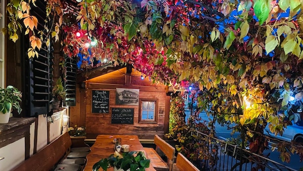 An outdoor seating area with a wooden table and benches, surrounded by foliage and a wooden structure with signage. - Hotel Sternen Worb (Worb)