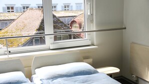 Een hotelkamer met twee bedden, een raam met uitzicht op gebouwen en een radiator.