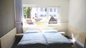 Een kamer met een bed, een klein tafeltje en een raam met uitzicht op gebouwen.