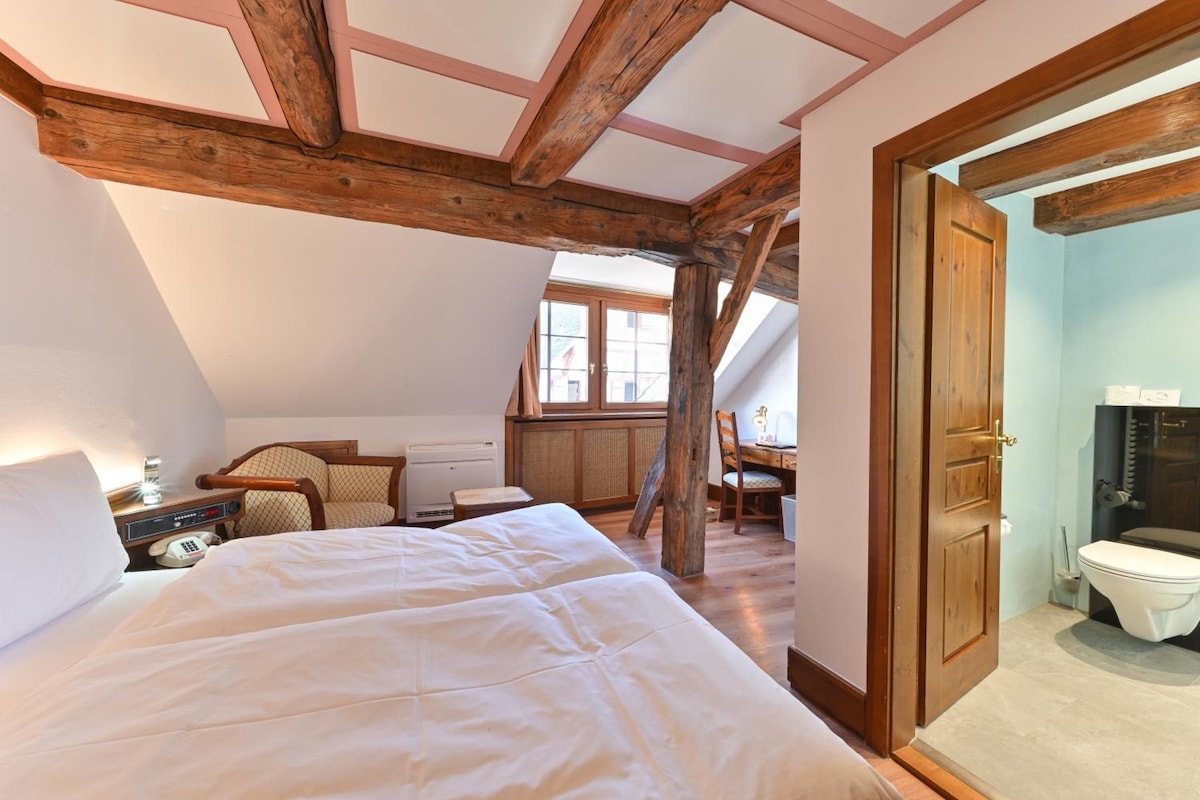 Un dormitorio con una cama grande, un escritorio y una silla. Se ve una ventana y una puerta.