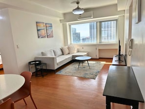 A modern living room with a sofa, a small round table, a dining table with chairs, and a large window with a city view. - Grand Cenia Residence with 2 Bedrooms Condo Unit (Cebu City)