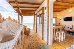 A wooden deck with a hammock, a dining area with a table and chairs, and a TV mounted on the wall. - B4 Boutique (Paje)