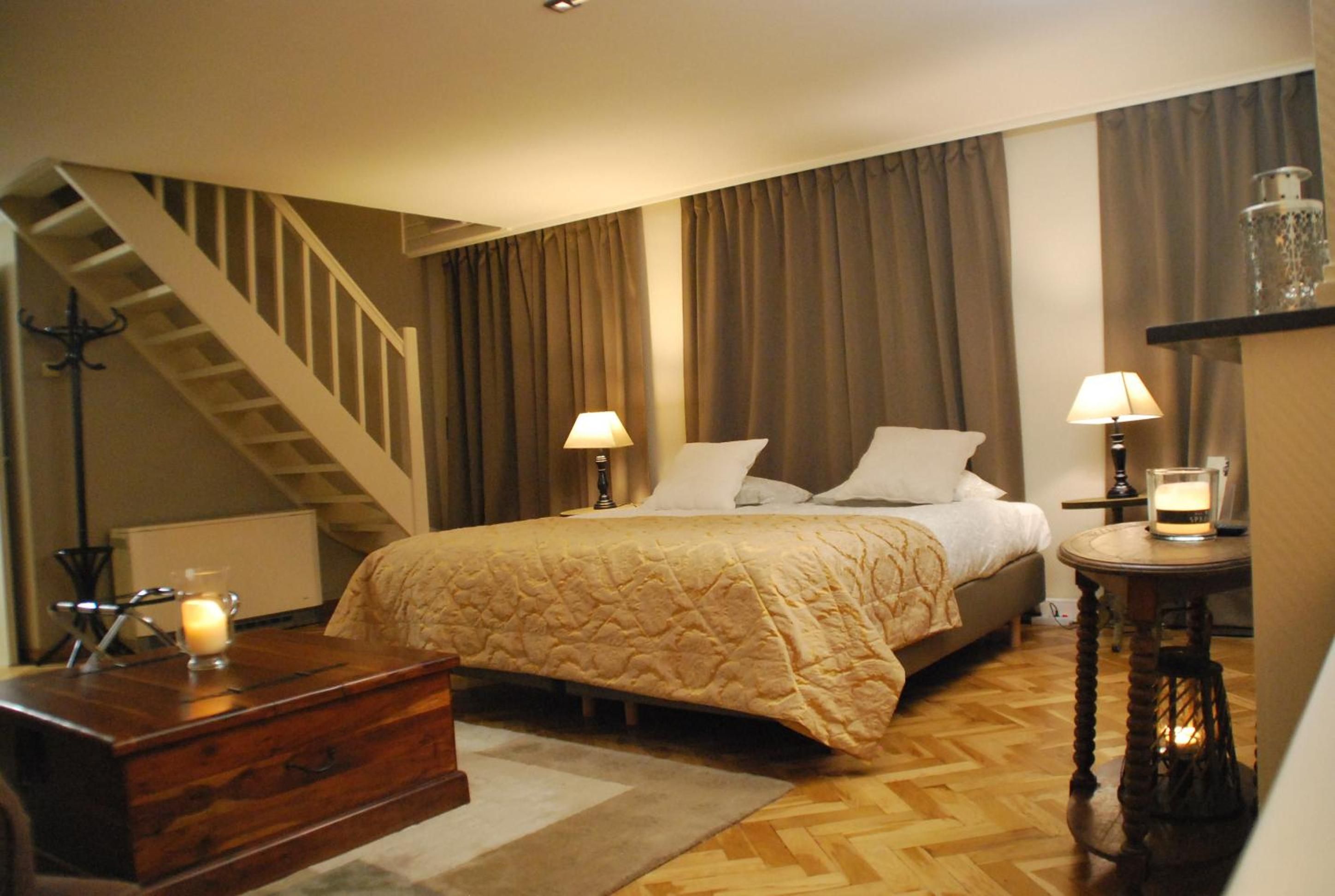 Een hotelkamer met een bed, twee bedlampen, een houten dressoir, een klein tafeltje met een kaars en een trap.