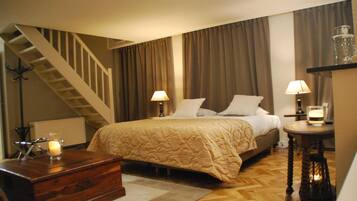 Een hotelkamer met een bed, twee bedlampen, een houten dressoir, een klein tafeltje met een kaars en een trap.