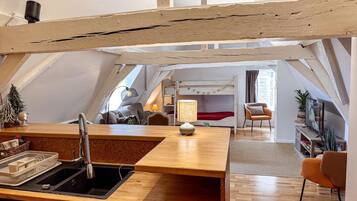 Een loft-achtige kamer met een keuken, een eettafel en een gezellige zithoek met een bed.