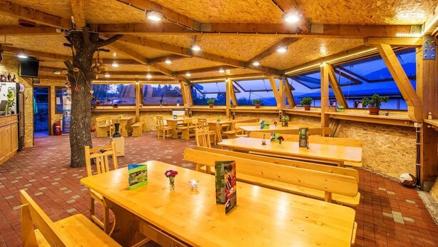 A wooden interior with tables and benches, large windows, and a tree. - Debeli Dab (Kresna)