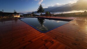 A wooden deck with a swimming pool, surrounded by buildings and trees, under a clear sky. - Debeli Dab (Kresna)