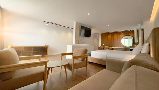 Una habitación de hotel moderna con una cama, dos sofás, una mesita y un televisor.