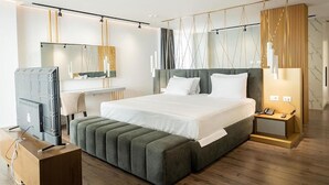 Una habitación de hotel moderna con una cama grande, televisión, escritorio y mesita de noche con teléfono.