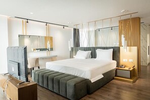 A modern hotel room with a large bed, a television, a desk, and a bedside table with a phone. - Dorchester Hotel (Ksamil)