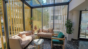 Un interior moderno con techo de vidrio, un sofá beige, un sillón verde y una pequeña mesa.