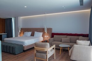 A modern hotel room with a bed, a sofa, a small table, and a chair. - Dorchester Hotel (Ksamil)