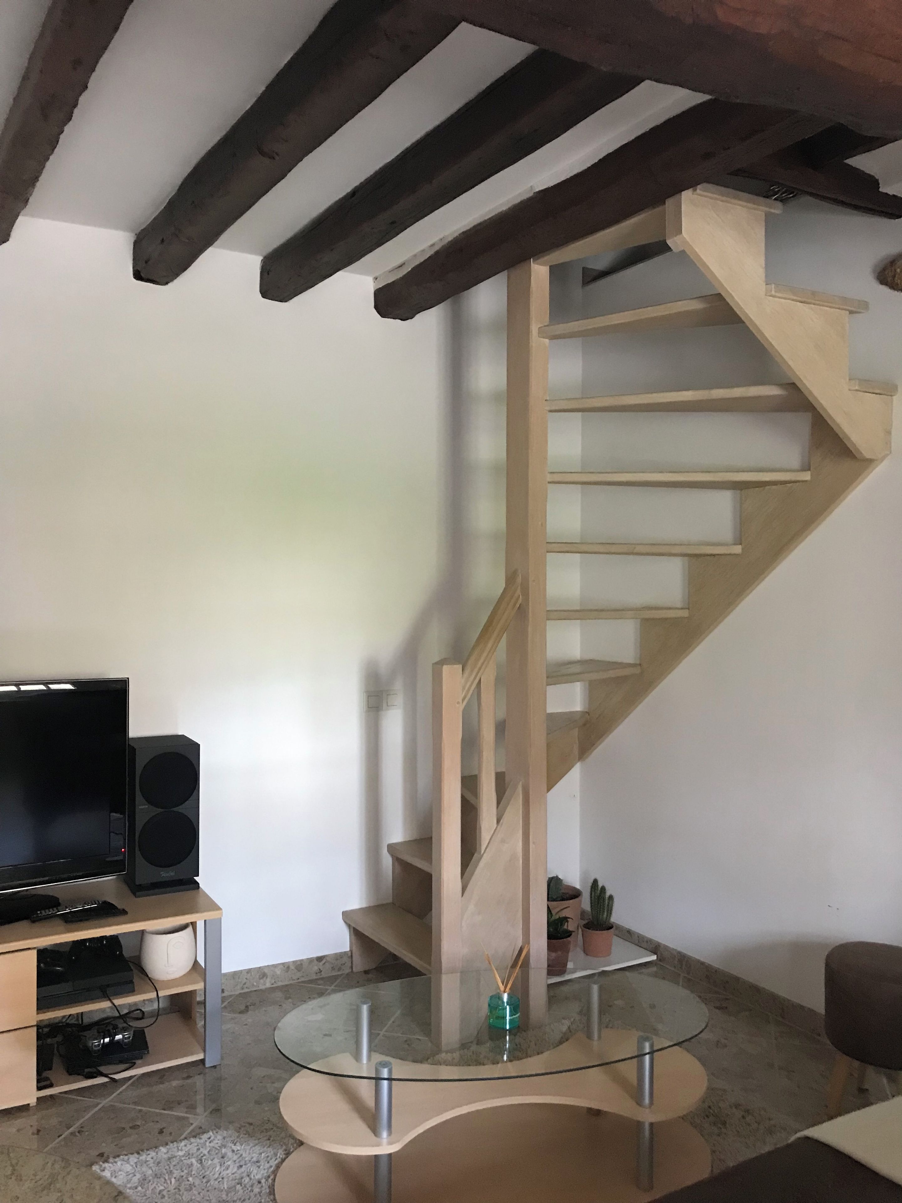 A living room with a wooden staircase, a flat-screen TV, a speaker, and a glass coffee table.