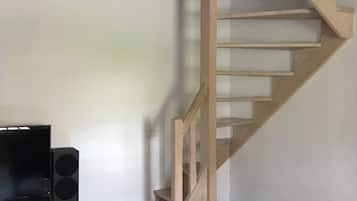 A living room with a wooden staircase, a flat-screen TV, a speaker, and a glass coffee table.