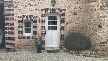 A building with a stone facade, a white door, and two windows with shutters.