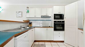 A compact kitchen with white cabinetry, a stainless steel sink, a microwave, and an oven. - Sea Views on Kennedy (South Mission Beach)