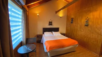 Una habitación de hotel con una cama, una mesita, una silla y una pared de madera.
