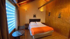 A hotel room with a bed, a small table, a chair, and a wooden wall. - Patagonia Bordelago (Río Ibáñez)