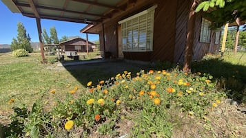 Una cabaña de madera con un porche cubierto y un jardín lleno de flores amarillas.