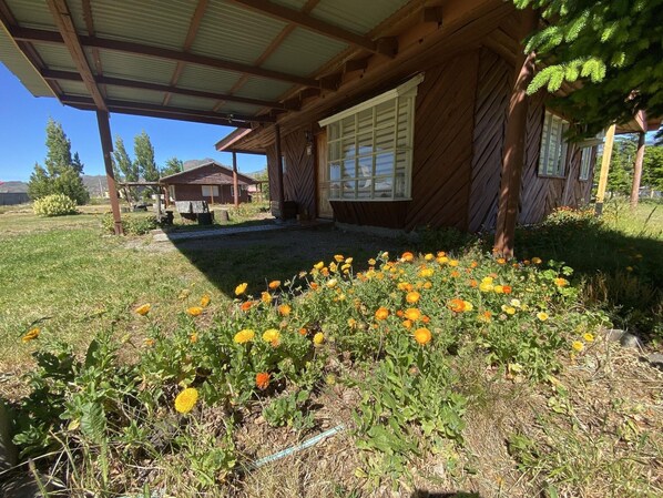 A wooden cabin with a covered porch and a garden with yellow flowers. - Patagonia Bordelago (Río Ibáñez)