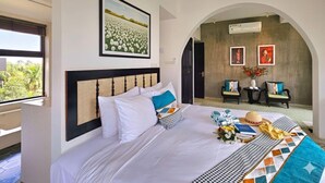 Een hotelkamer met een groot bed, uitzicht door een boogvormige doorgang en een ingelijst schilderij aan de muur.