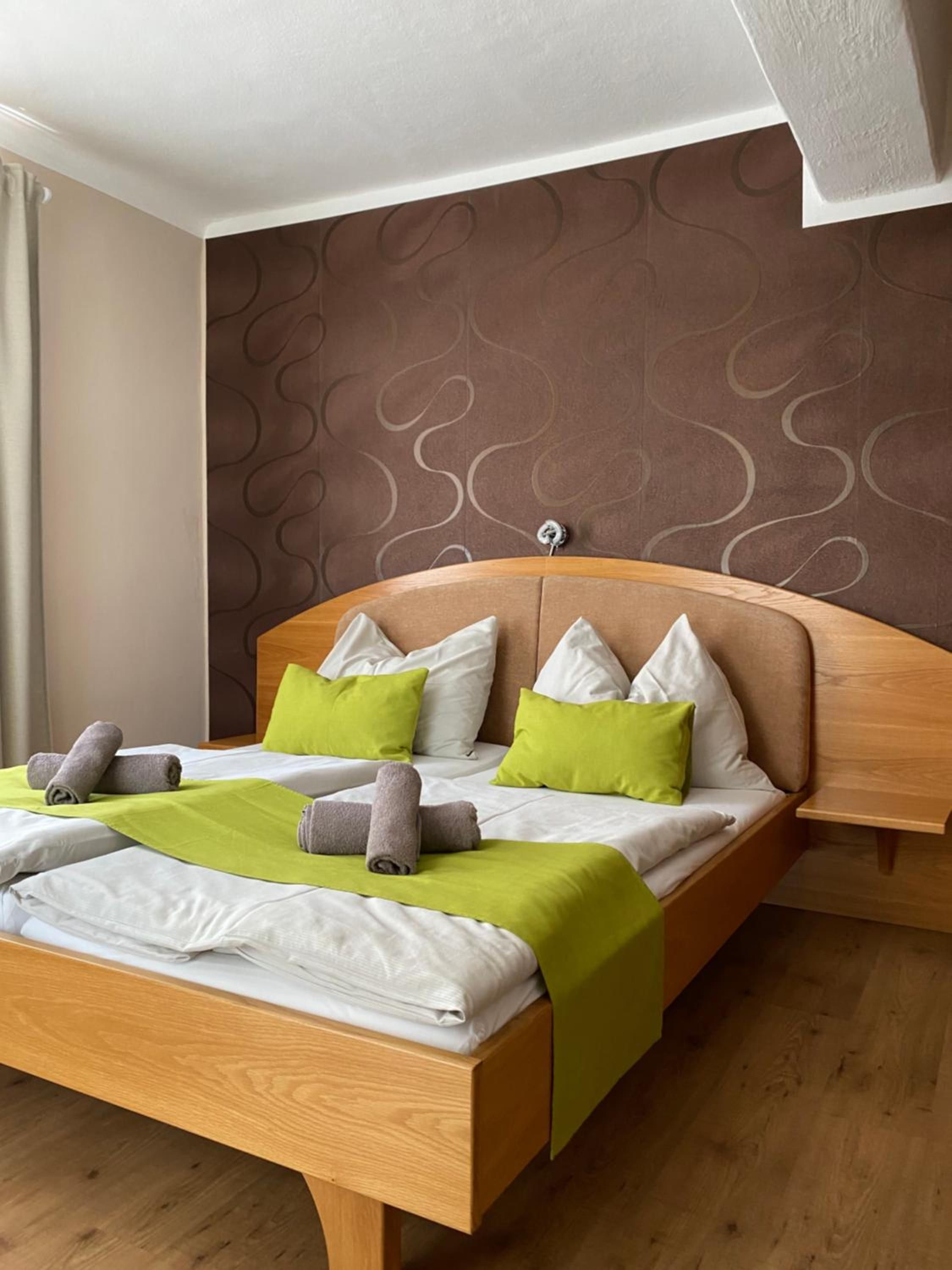 Une chambre d’hôtel avec un lit en bois, une literie verte et blanche, et un mur orné d’un motif.