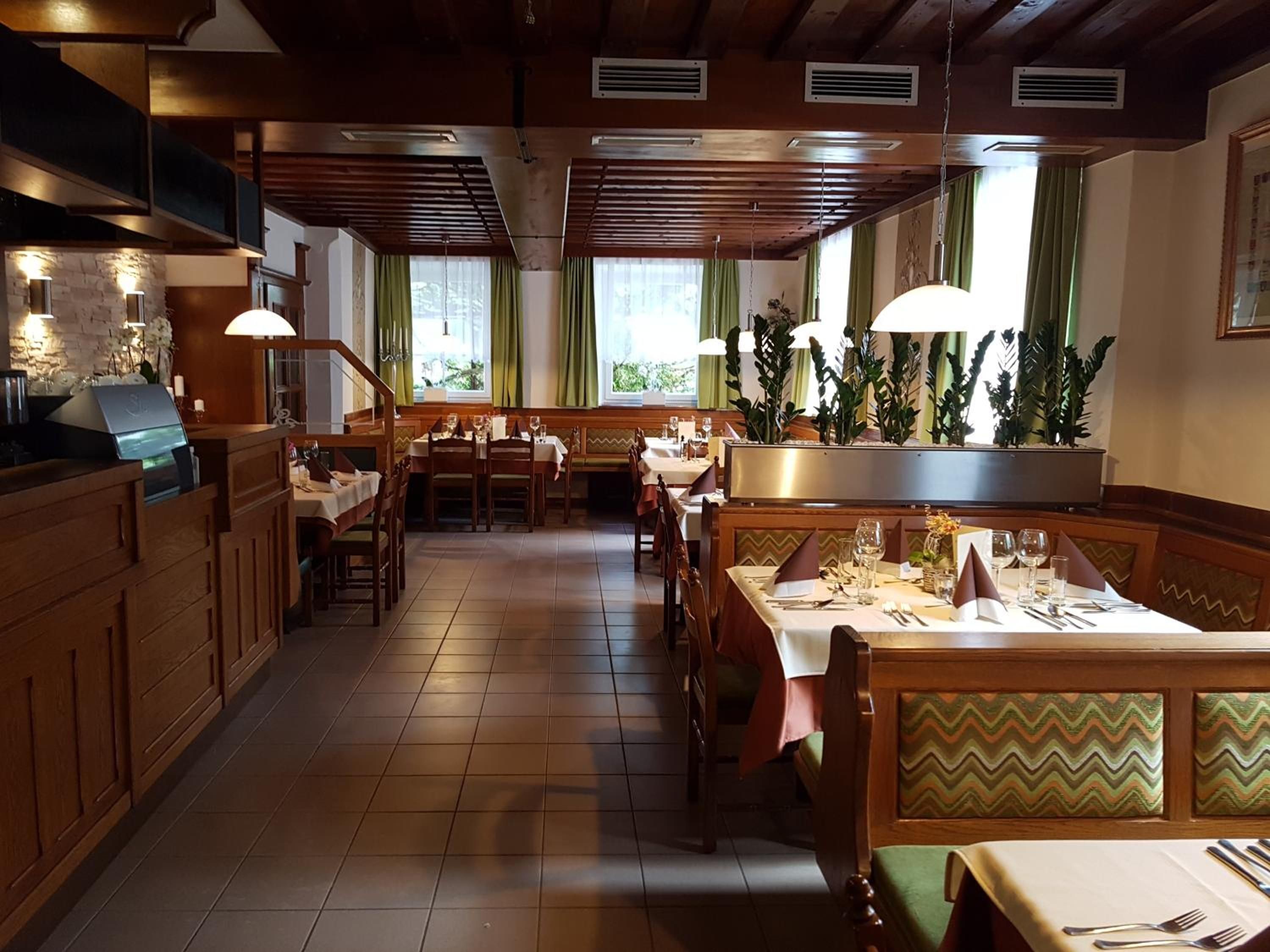 L’intérieur d’un restaurant, avec des meubles en bois, des tables dressées pour le service et de grandes fenêtres ornées de rideaux.