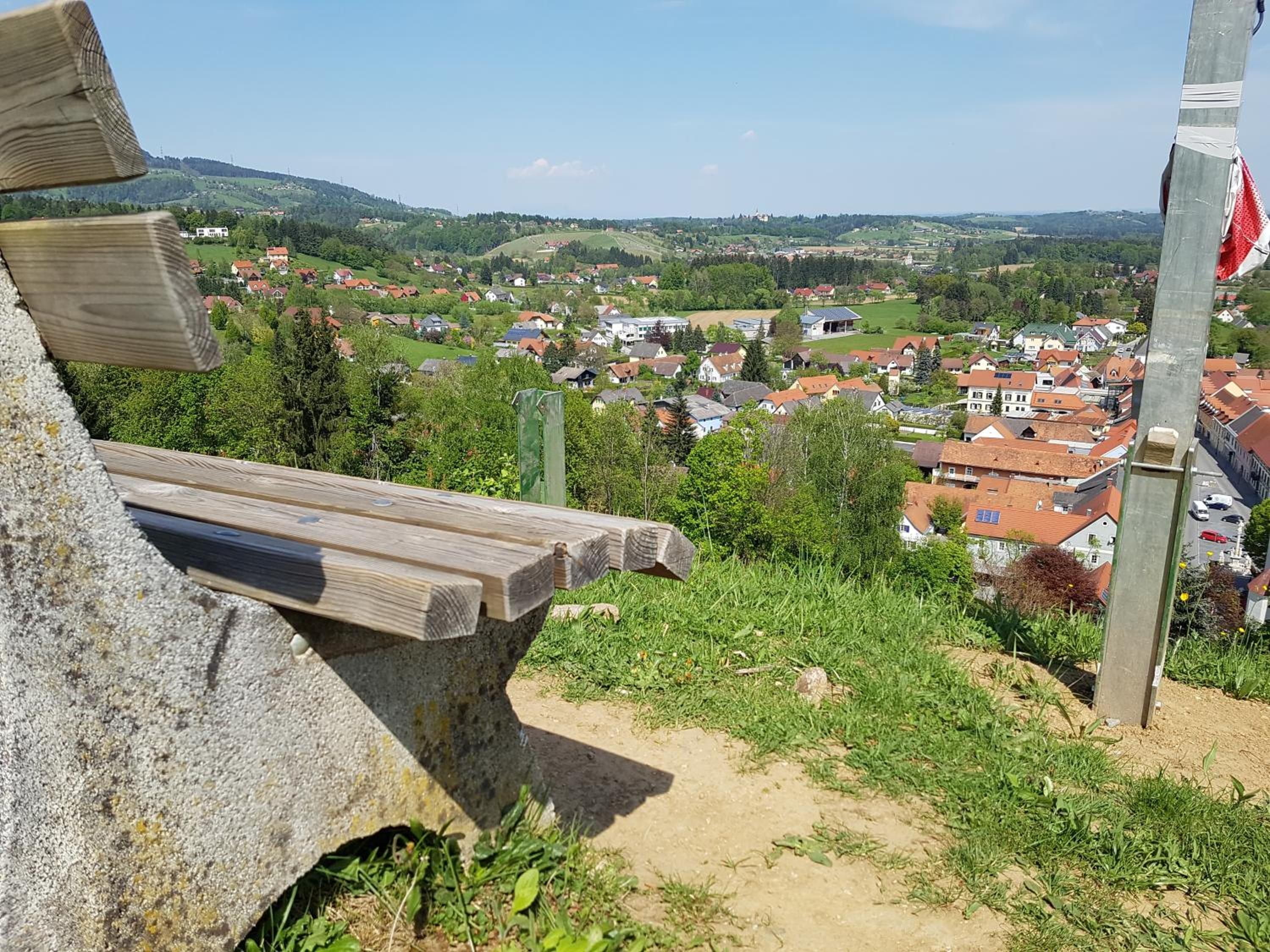 Un banc de pierre donnant sur un village aux maisons aux toits rouges et à la végétation luxuriante.